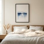 Serene watercolour painting with soft blue and grey washes depicting misty lake landscape, framed in black above bed